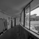 Graffiti-lined corridor in a deserted building, windows overlooking an abandoned complex – nbcreations