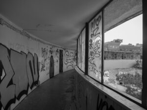 Graffiti-lined corridor in a deserted building, windows overlooking an abandoned complex – nbcreations