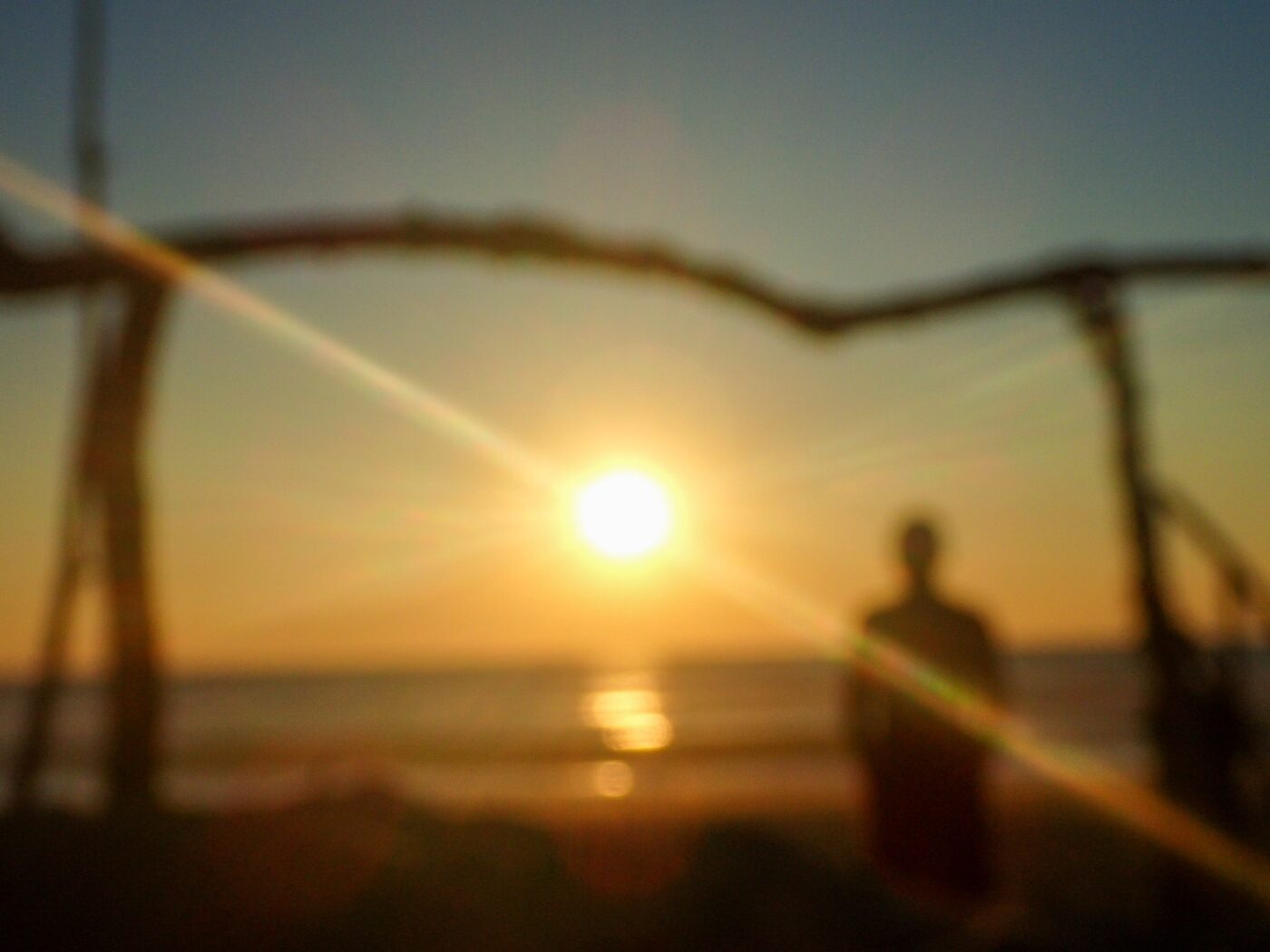 Artistic blurred image of a person on the beach at sunset, framed by branches with sun rays – poetic seaside scene - nbcreations