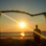 Artistic blurred image of a person on the beach at sunset, framed by branches with sun rays – poetic seaside scene - nbcreations
