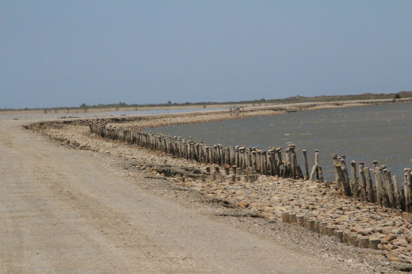 Dirt road alongside a salt marsh bordered by weathered wooden posts and stones – minimalist coastal landscape - nbcreations