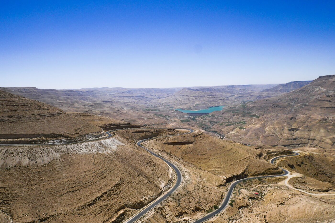 Winding road through arid mountain landscape with blue lake in the distance under a clear sky – panoramic desert view - nbcreations