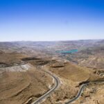 Winding road through arid mountain landscape with blue lake in the distance under a clear sky – panoramic desert view - nbcreations
