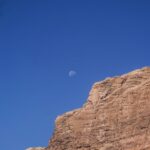 Three-quarter moon in broad daylight above a cliff with blue sky – daytime lunar scene - nbcreations