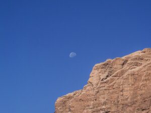 Three-quarter moon in broad daylight above a cliff with blue sky – daytime lunar scene - nbcreations