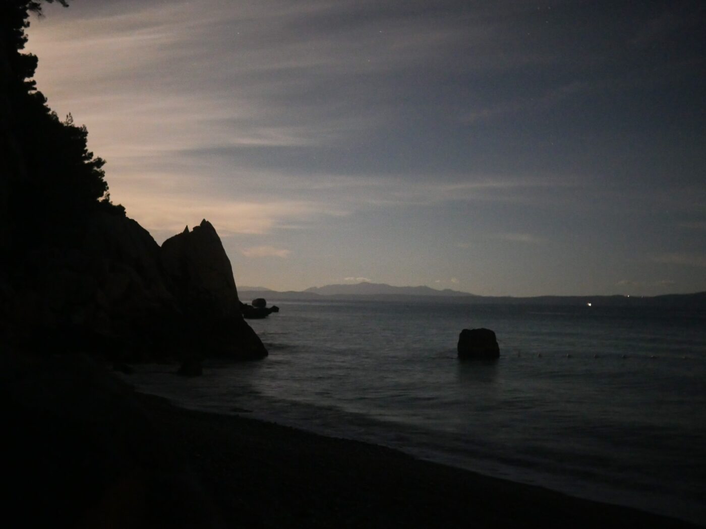 Glow of moonlight hidden behind a rocky coastline at night – luminous coastal silhouette - nbcreations