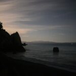 Glow of moonlight hidden behind a rocky coastline at night – luminous coastal silhouette - nbcreations