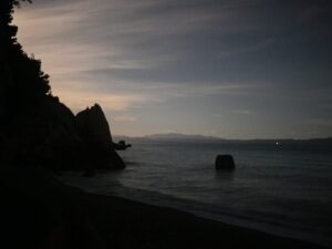 Glow of moonlight hidden behind a rocky coastline at night – luminous coastal silhouette - nbcreations