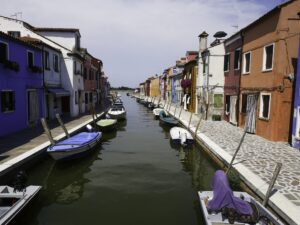 Canal in Murano lined with colorful houses and moored boats – Venetian island scene - nbcreations