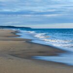 Sandy beach with a distant solitary walker on the horizon – minimal coastal scene - nbcreations