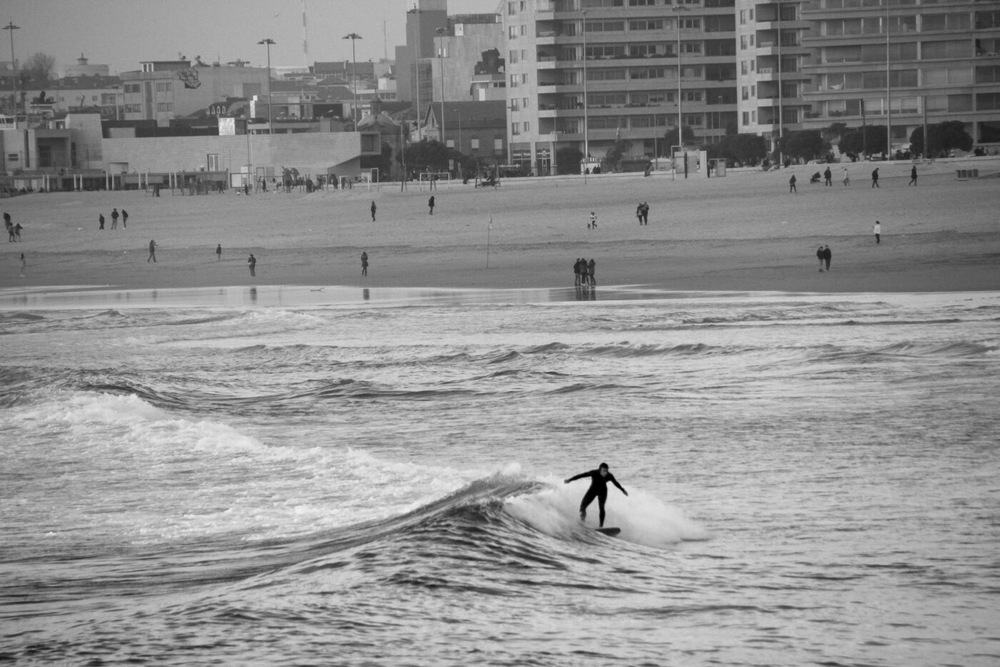 Black and white side view of a surfer riding a wave toward the beach – minimalist surf scene - nbcreations