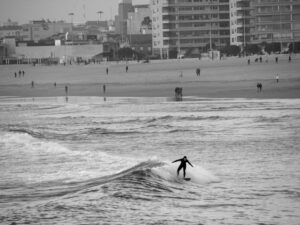 Black and white side view of a surfer riding a wave toward the beach – minimalist surf scene - nbcreations