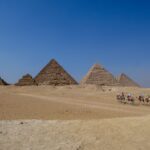 Giza pyramid with tourists riding camels toward the monument – Egypt desert scene - nbcreations