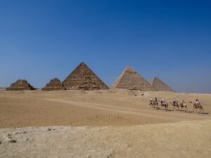 Giza pyramid with tourists riding camels toward the monument – Egypt desert scene - nbcreations