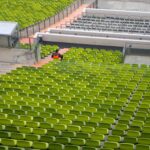 Person in orange vest sitting alone among empty green stadium seats at Munich’s Olympiastadion