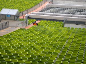 Person in orange vest sitting alone among empty green stadium seats at Munich’s Olympiastadion