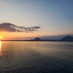 Sunset over a calm lake with distant mountains and gentle clouds – nbcreations