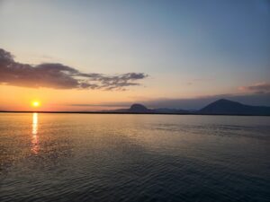 Sunset over a calm lake with distant mountains and gentle clouds – nbcreations