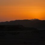 Silhouette of rocky desert hills at sunset with an orange sky and a tiny lone figure – nbcreations