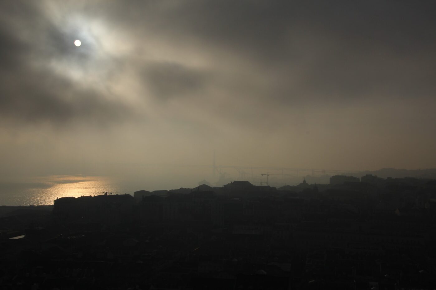 Sun breaking through heavy morning fog over a city skyline, golden reflection on water – nbcreations