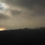 Sun breaking through heavy morning fog over a city skyline, golden reflection on water – nbcreations