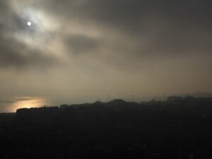 Sun breaking through heavy morning fog over a city skyline, golden reflection on water – nbcreations