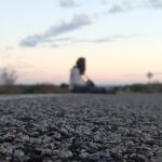 Close-up of asphalt with a person sitting blurred in the distance on a road at dusk – nbcreations