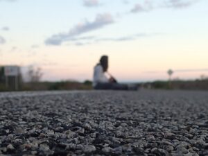 Close-up of asphalt with a person sitting blurred in the distance on a road at dusk – nbcreations