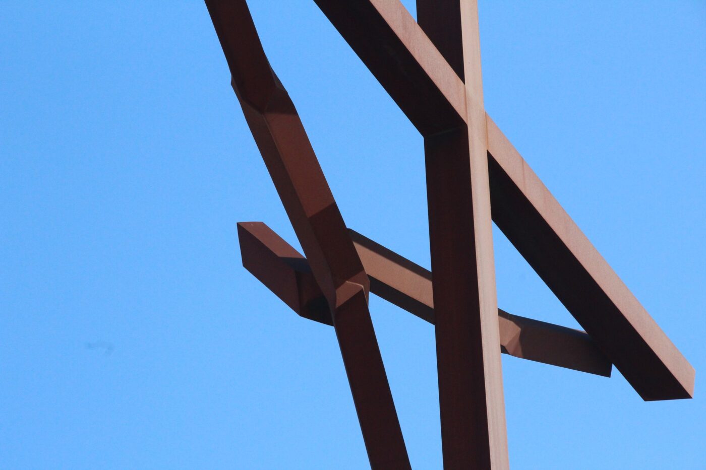 Close-up of a large rust-colored metal cross of jesusu against blue sky – nbcreations