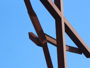Close-up of a large rust-colored metal cross of jesusu against blue sky – nbcreations