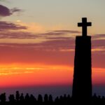 Silhouette of a cross monument at sunset with people gathered – nbcreations