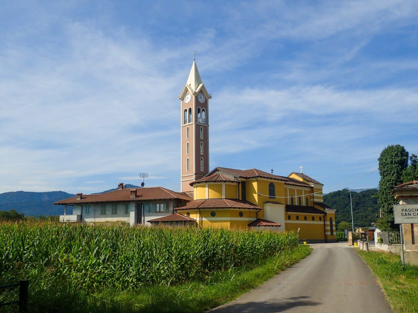 Church with a tall bell tower in a rural Italian village, surrounded by cornfields under a blue sky. - nbcreations
