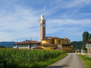 Church with a tall bell tower in a rural Italian village, surrounded by cornfields under a blue sky. - nbcreations