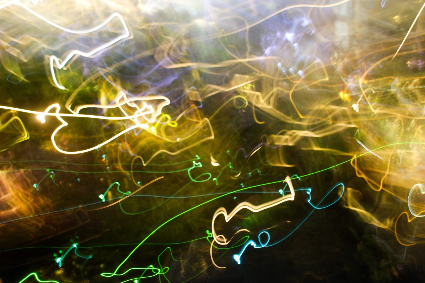 Abstract light painting with green, yellow, and white trails on a dark background.- nbcreations