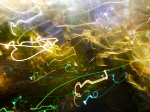 Abstract light painting with green, yellow, and white trails on a dark background.- nbcreations