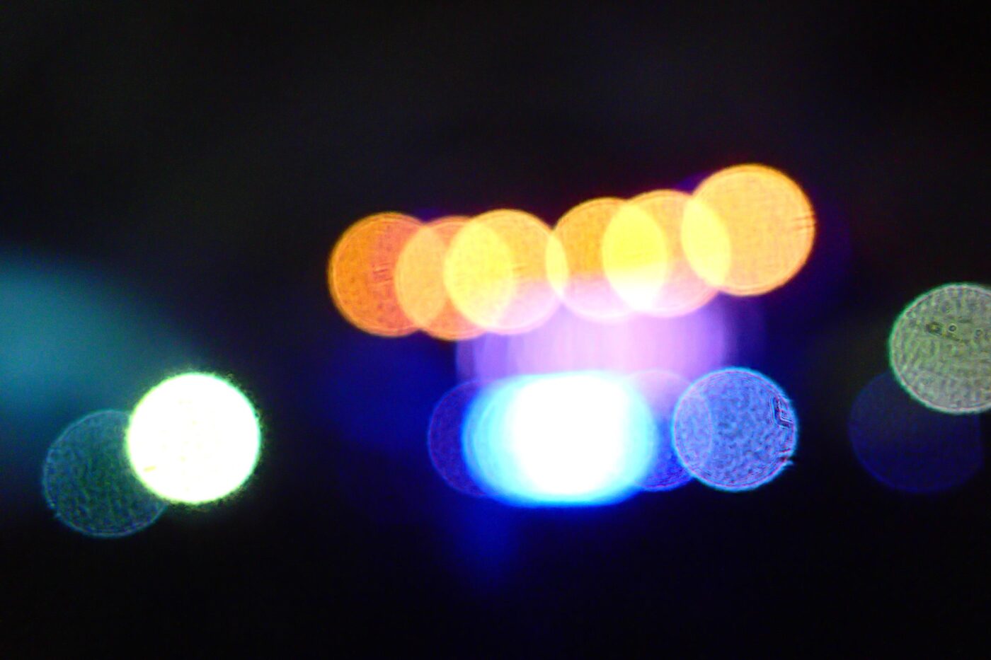 Abstract bokeh lights with blue, orange, and green circles on a black background.- nbcreations