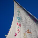 White sail decorated with colorful flags against a deep blue sky – nbcreations– Nile river scene - nbcreations