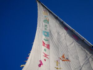 White sail decorated with colorful flags against a deep blue sky – nbcreations– Nile river scene - nbcreations